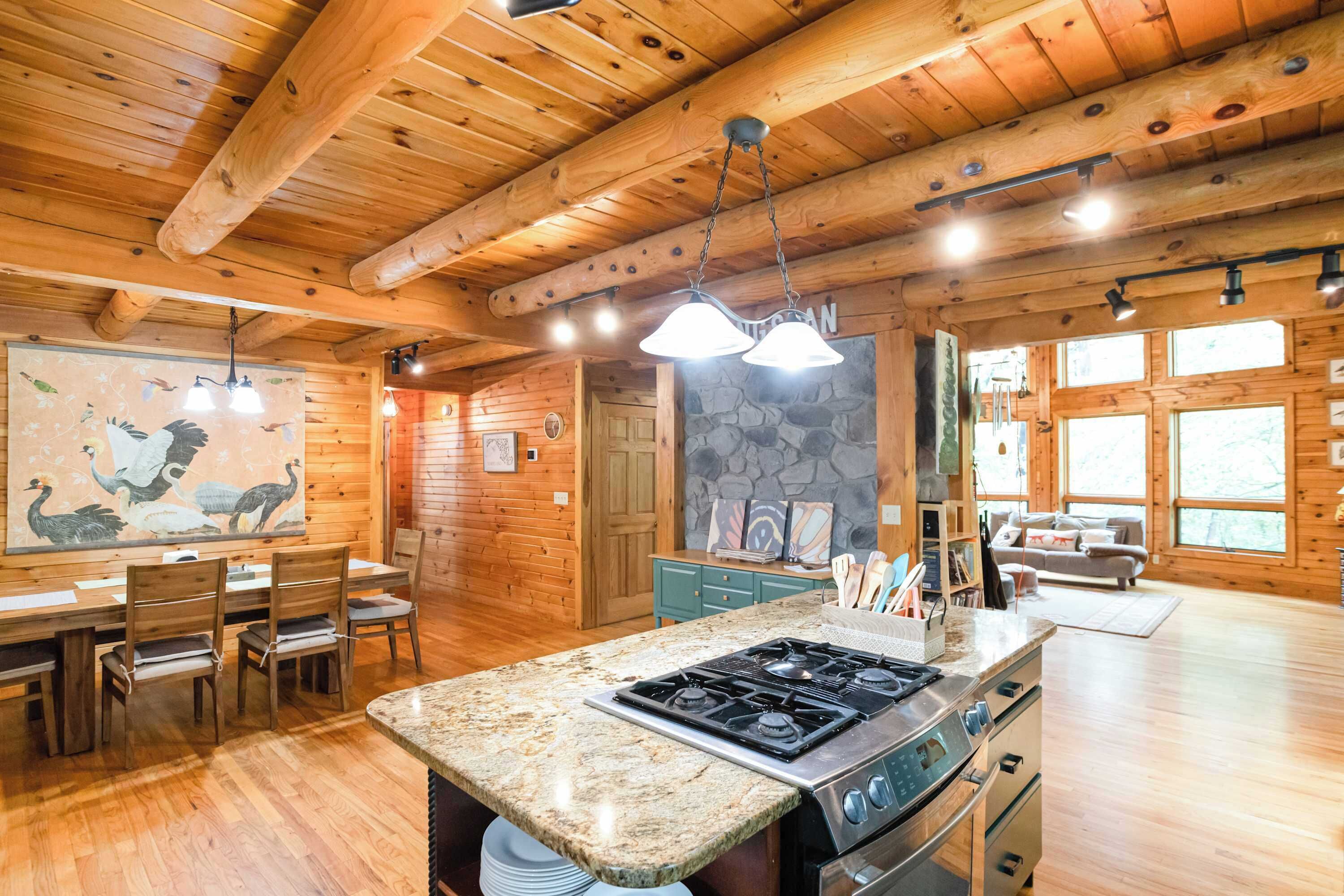 A wooden cabin interior with a kitchen featuring a granite countertop, stainless steel appliances, and a dining area with wooden chairs and a table.