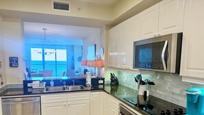 A modern kitchen with white cabinets, stainless steel appliances, and a large window overlooking a balcony. - Beach Colony West 10E 2BR Gulf Front 2/Beach Service & Onsite Management (Navarre)