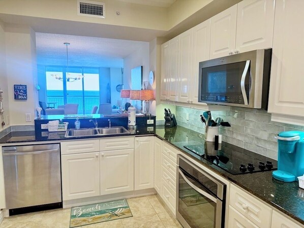 A modern kitchen with white cabinets, stainless steel appliances, and a large window overlooking a balcony. - Beach Colony West 10E 2BR Gulf Front 2/Beach Service & Onsite Management (Navarre)