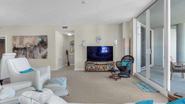 A spacious living room with a large flat-screen TV, comfortable seating, and a view through a sliding glass door. - Beach Colony West 10E 2BR Gulf Front 2/Beach Service & Onsite Management (Navarre)
