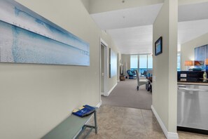 A hotel hallway with a large abstract painting on the left, a bench with a book, and a view into a dining area with chairs and a table.