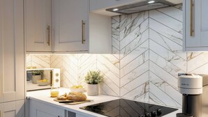 A modern kitchen with white cabinets, a black induction cooktop, and a Nespresso machine. - The Devonshire Suite - Your 5 Star West End Stay! (Glasgow)