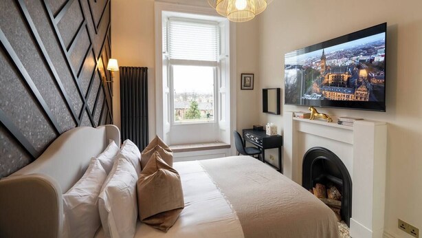 A modern hotel room with a large bed, a fireplace, a television, and a cityscape view. - The Devonshire Suite - Your 5 Star West End Stay! (Glasgow)