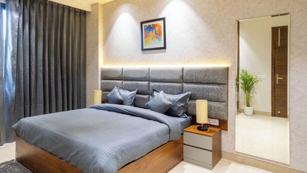Quarto moderno com uma cama grande, cabeceira, mesas de cabeceira, um espelho e uma pintura na parede.