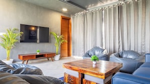 A modern living room with a wooden coffee table, leather sofas, a flat-screen TV mounted on the wall, and two potted plants. - Housr Sector 56 Gurgaon Sushant Lok 2 (Gurugram)