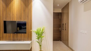 Um interior moderno com painel de madeira, televisão fixada na parede, planta em vaso e corredor que leva a uma porta.