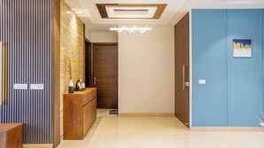 A modern hotel lobby with a wooden reception desk, a blue door, and a ceiling light fixture. - Housr Sector 56 Gurgaon Sushant Lok 2 (Gurugram)