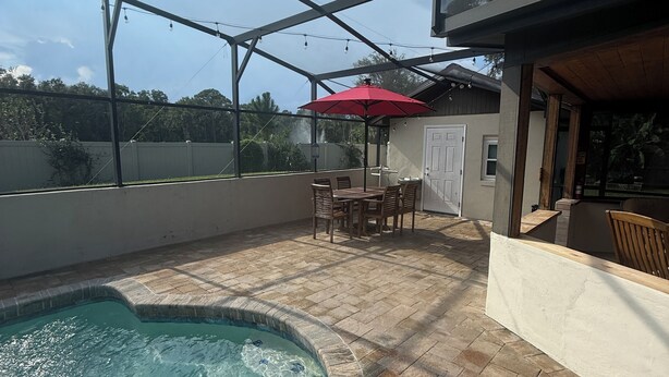 Un espace extérieur abrité comprenant une piscine, du mobilier de jardin et un parasol rouge.