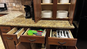 Une cuisine dotée de plans de travail en granit, de meubles en bois et d’un système de rangement intégré pour les tiroirs, comprenant des ustensiles.