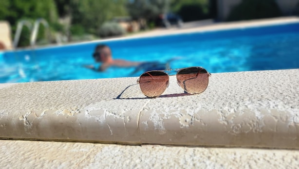 A pair of sunglasses on a textured surface near a pool.