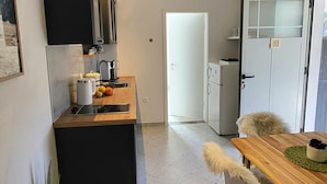 A compact kitchen with a central island, a dining table with a furry chair, and a refrigerator.