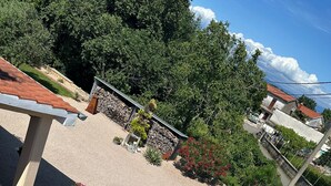 A courtyard with a paved area, a stone wall, and various potted plants.