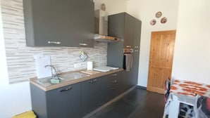 A compact kitchen with dark cabinets, a sink, and a wooden door. - Ana&julio holiday home (Valledoria)