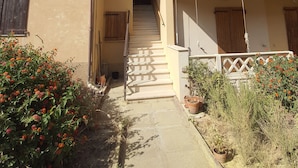 A two-story building with a central staircase leading to an upper floor. There are potted plants and flowers in the foreground. - Ana&julio holiday home (Valledoria)