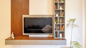 Una sala de estar moderna con un televisor de pantalla plana sobre una consola de madera, un panel de madera vertical y una estantería empotrada con objetos decorativos.