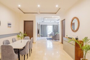 A modern hotel room with a dining area, a wooden reception desk, and a large mirror.