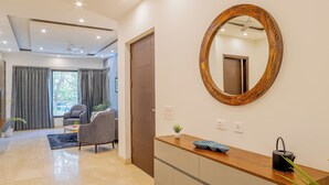 Habitación de hotel moderna con un tocador de madera, un espejo redondo y vista al área de estar.