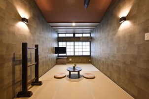Una habitación con tatami, una mesa baja, cojines y un televisor montado en la pared.