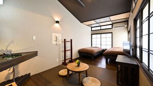 A traditional Japanese-style room with tatami flooring, a low wooden table, a cushioned bench, and a television. - Wooribow Ryokan (Kusatsu)