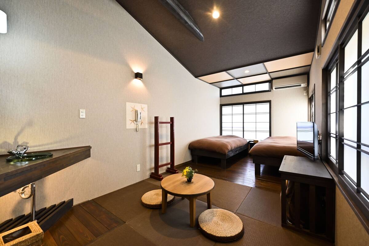 Una habitación tradicional japonesa con suelo de tatami, una mesa de madera baja, un banco acolchado y un televisor.