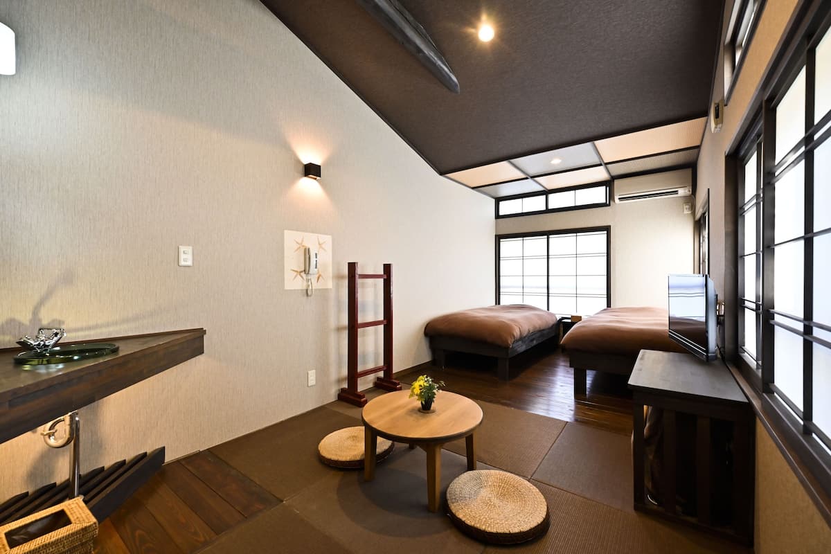 A traditional Japanese-style room with tatami flooring, a low wooden table, a cushioned bench, and a television.