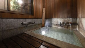 A wooden room with a hot spring bath, a window with bamboo outside, and a stone wall. - Wooribow Ryokan (Kusatsu)
