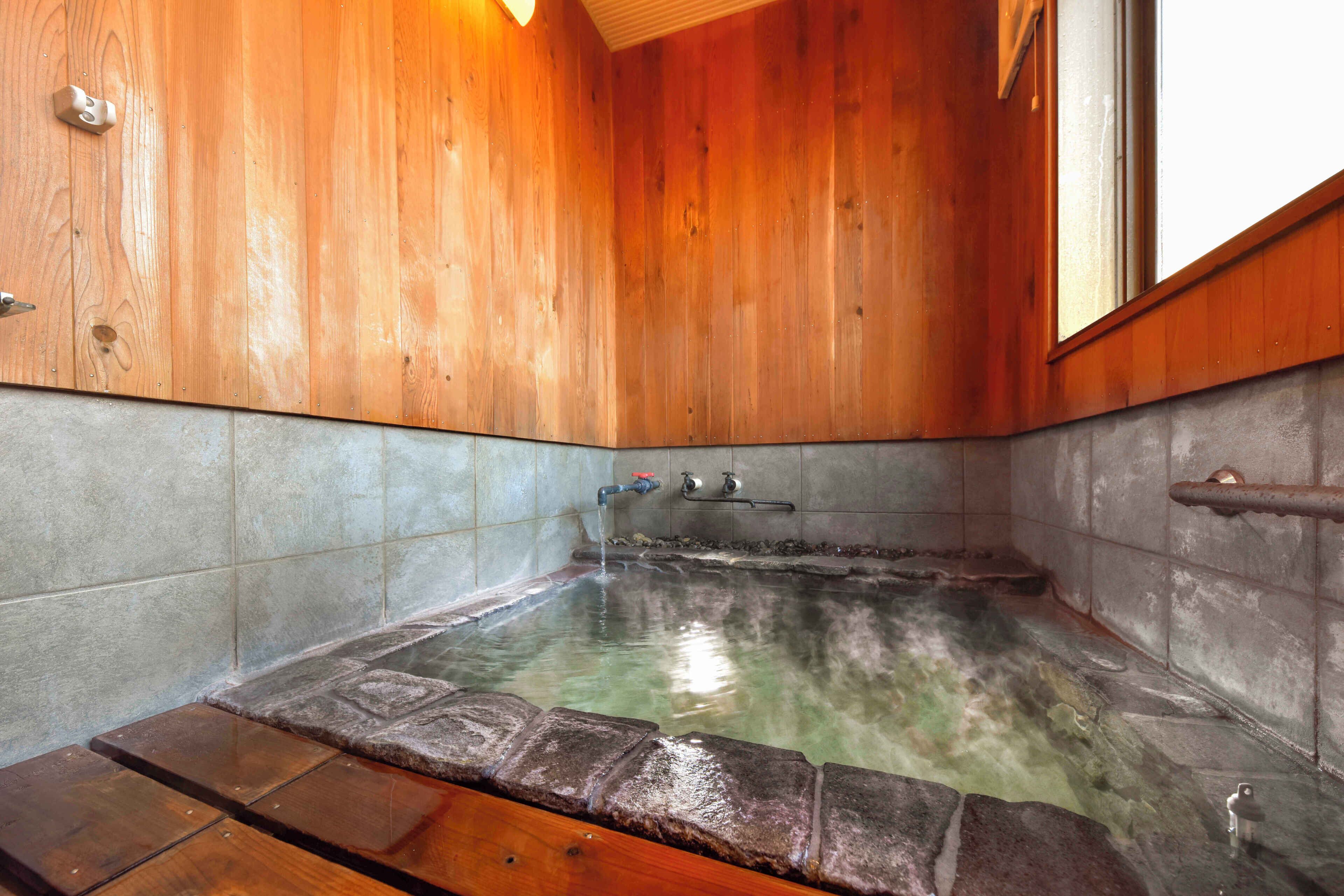 Un intérieur en bois avec un bain à remous carrelé en pierre, un banc en bois et une fenêtre.