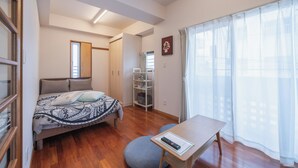 A bedroom with a bed, a desk, a chair, a wardrobe, a shelf, and a window with curtains. - Casa Leo Asato (Naha)