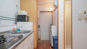 A compact kitchen with a microwave, stove, sink, and cabinets. - Casa Leo Asato (Naha)