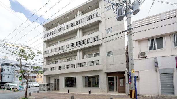 A multi-story building with balconies, a ground-level entrance, and a visible storefront. - Casa Leo Asato (Naha)