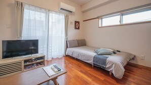 A bedroom with a bed, a TV, a window, and a wooden floor. - Casa Leo Asato (Naha)