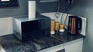 Een keuken met een magnetron, een koffiezetapparaat en een pak keukenpapier op het aanrecht.