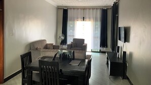 Een woonkamer met een eettafel, twee banken, een televisie en een ventilator.