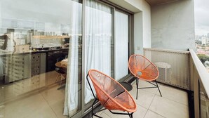 En balkon med to orange stole, en glasdør og udsigt over byen.