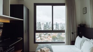 Et hotelværelse med et stort vindue, en seng, et natbord og et klædeskab.