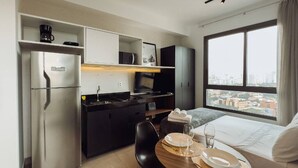Et kompakt hotelværelse med tekøkken, en seng med byudsigt og et spiseområde med et bord dækket til to.