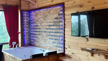 A wooden cabin interior with a wooden ceiling, a brick wall with a blue light strip, a wooden bar, and a large window.