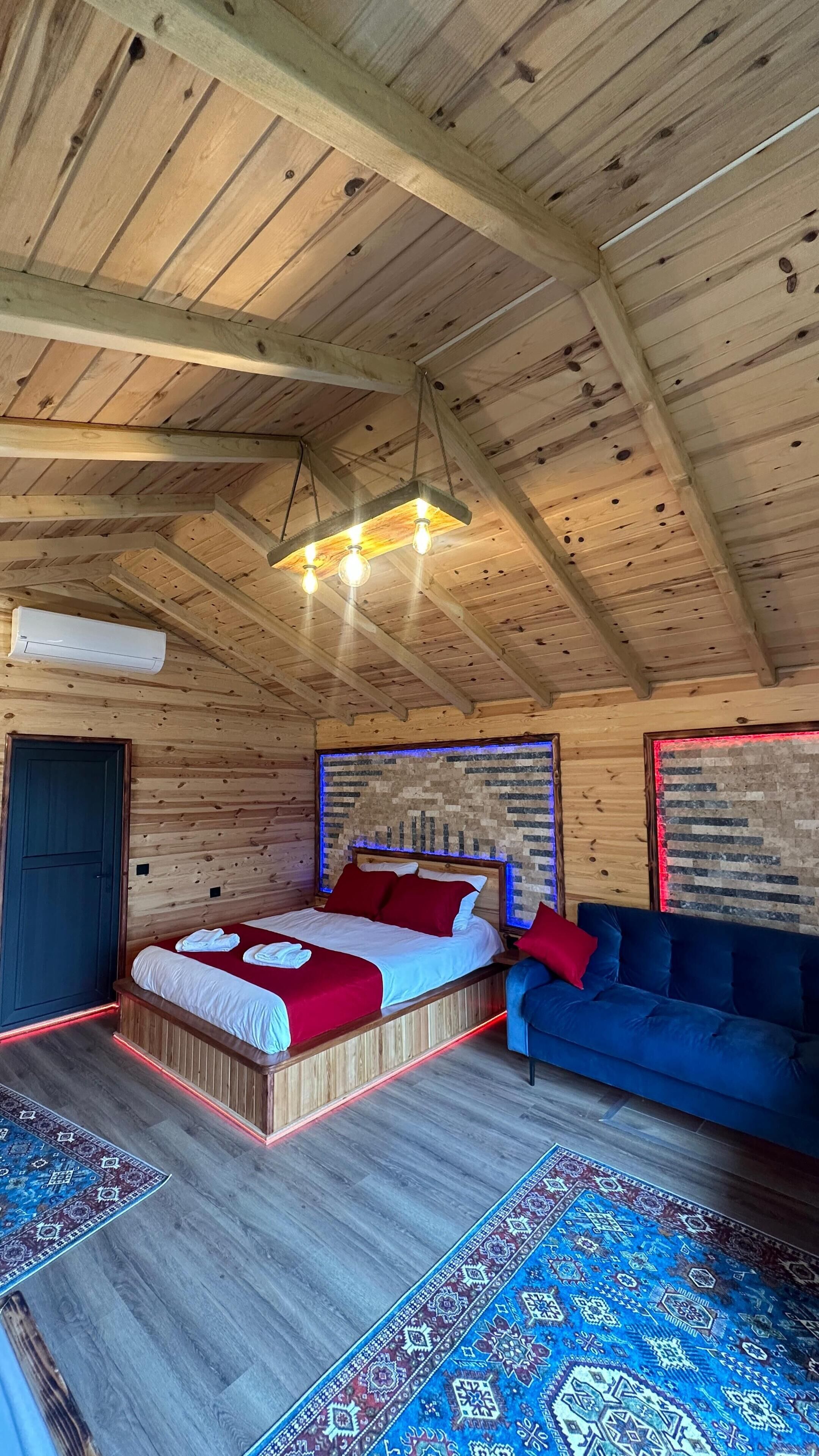 L’intérieur d’un chalet en bois, avec un lit, un canapé bleu, des tapis à motifs et un luminaire suspendu.