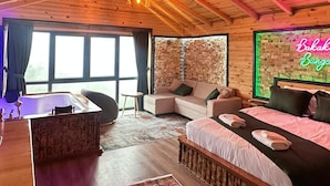 Een gezellig houten blokhutinterieur met een groot bed, een bank, een eettafel en een stenen muur.