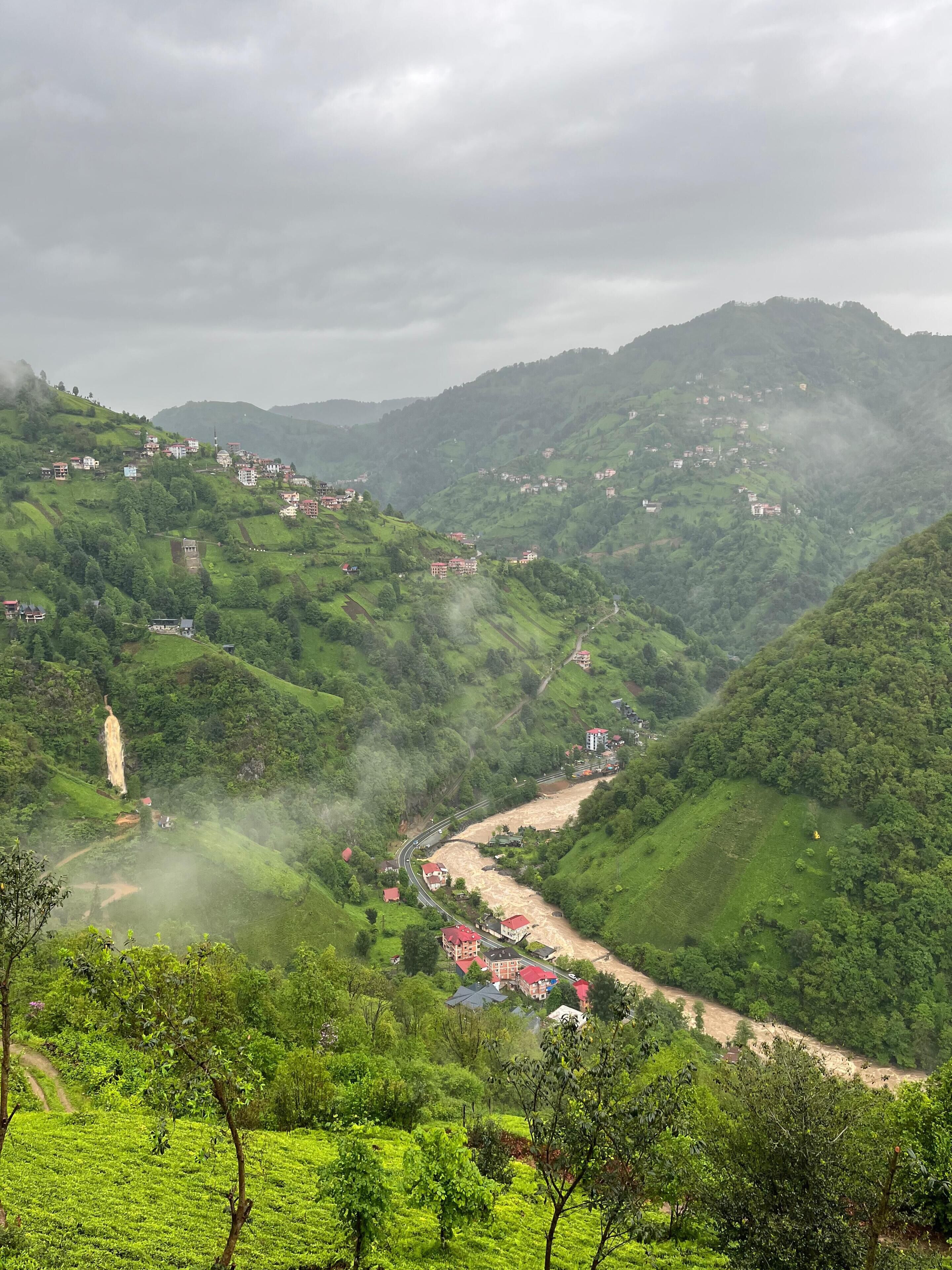 Eine hügelige Landschaft mit verstreuten Gebäuden, einer kurvenreichen Straße und einem markanten Turm.