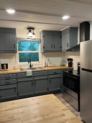 A modern kitchen with grey cabinets, stainless steel appliances, a wooden countertop, and a window providing a view of trees. - Noisy creekfront cabin in Marble! Pet friendly! Close to the casino (Marble)
