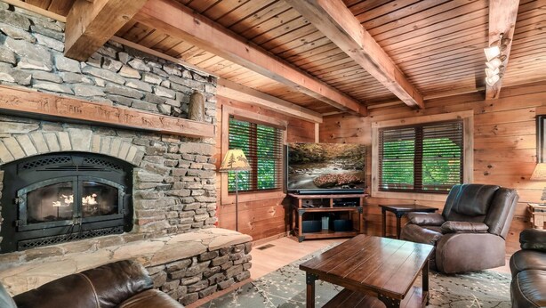 Ein gemütliches Blockhaushaus-Interieur mit Kamin aus Stein, Ledermöbeln und Holzbalken.