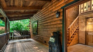 Eine Holzhütte mit Veranda, einer Bank, einer Holzskulptur und einer Treppe zum Haupteingang.