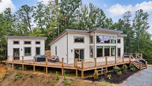 A modern two-story house with a deck, large windows, and a staircase leading to a second level. - 2BR Cabin with Private Indoor Pool and Hot Tub (Cosby)