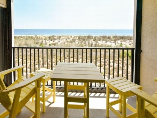 Un balcón con mesa y dos sillas, con vista a una playa de vegetación escasa y una vista despejada del océano.