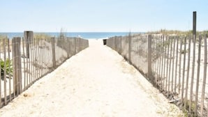 Ein Sandweg am Strand, gesäumt von Holzzäunen, der zum Meer führt.