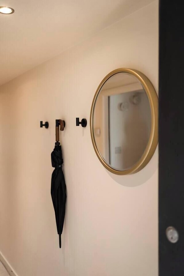 A bathroom with a round mirror, a black umbrella hanging on a hook, and a door with a round handle.