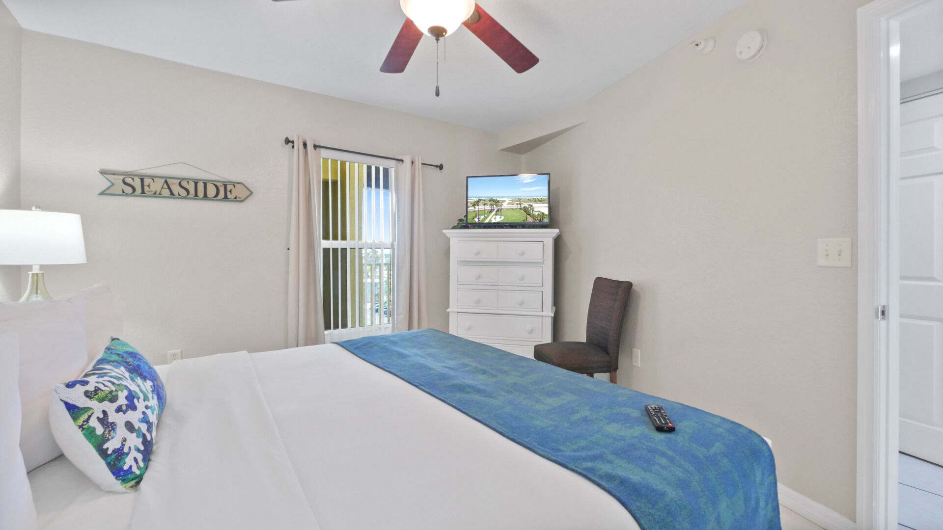 Ein Schlafzimmer mit Bett, Schminktisch, Stuhl, Fernseher und Deckenventilator.