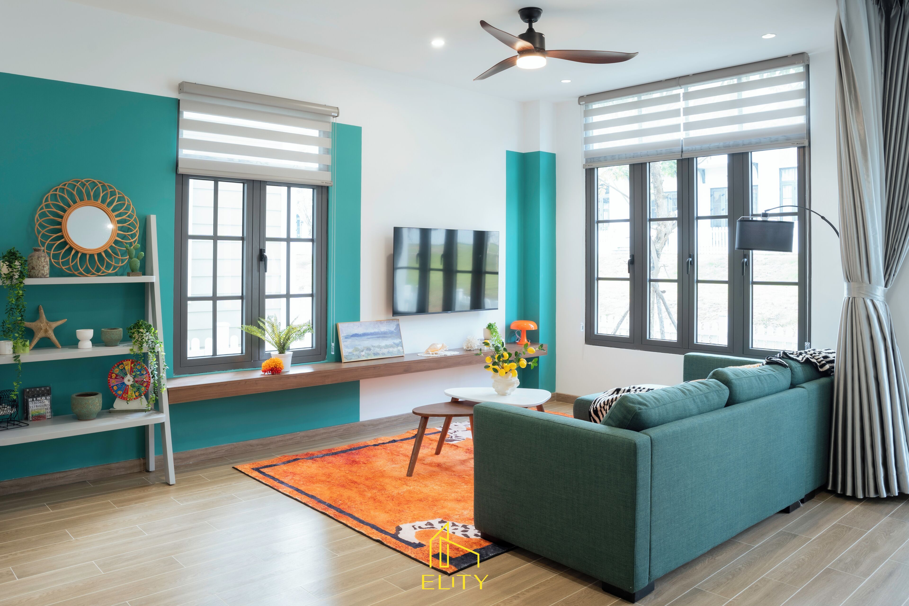 Een moderne woonkamer met blauwgroene muren, een groene bank, een houten vloer en een plafondventilator.