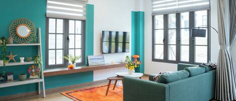Een moderne woonkamer met blauwgroene muren, een groene bank, een houten vloer en een plafondventilator.